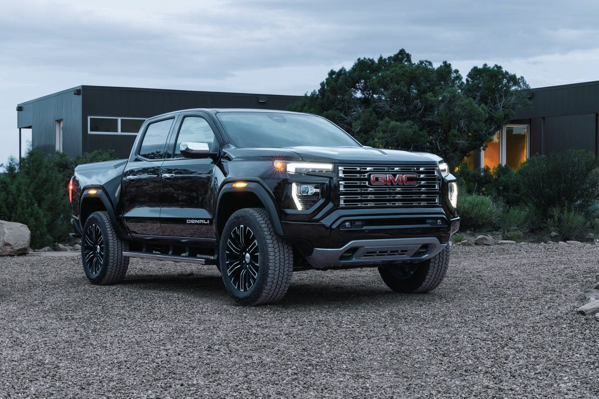 Black GMC Canyon Denali on a gravel drive, dark modern house behind it, evening light