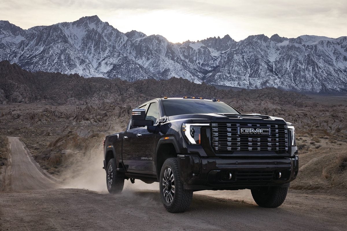 Black GMC Sierra HD Denali Ultimate on a gravel road with snow-capped mountains behind