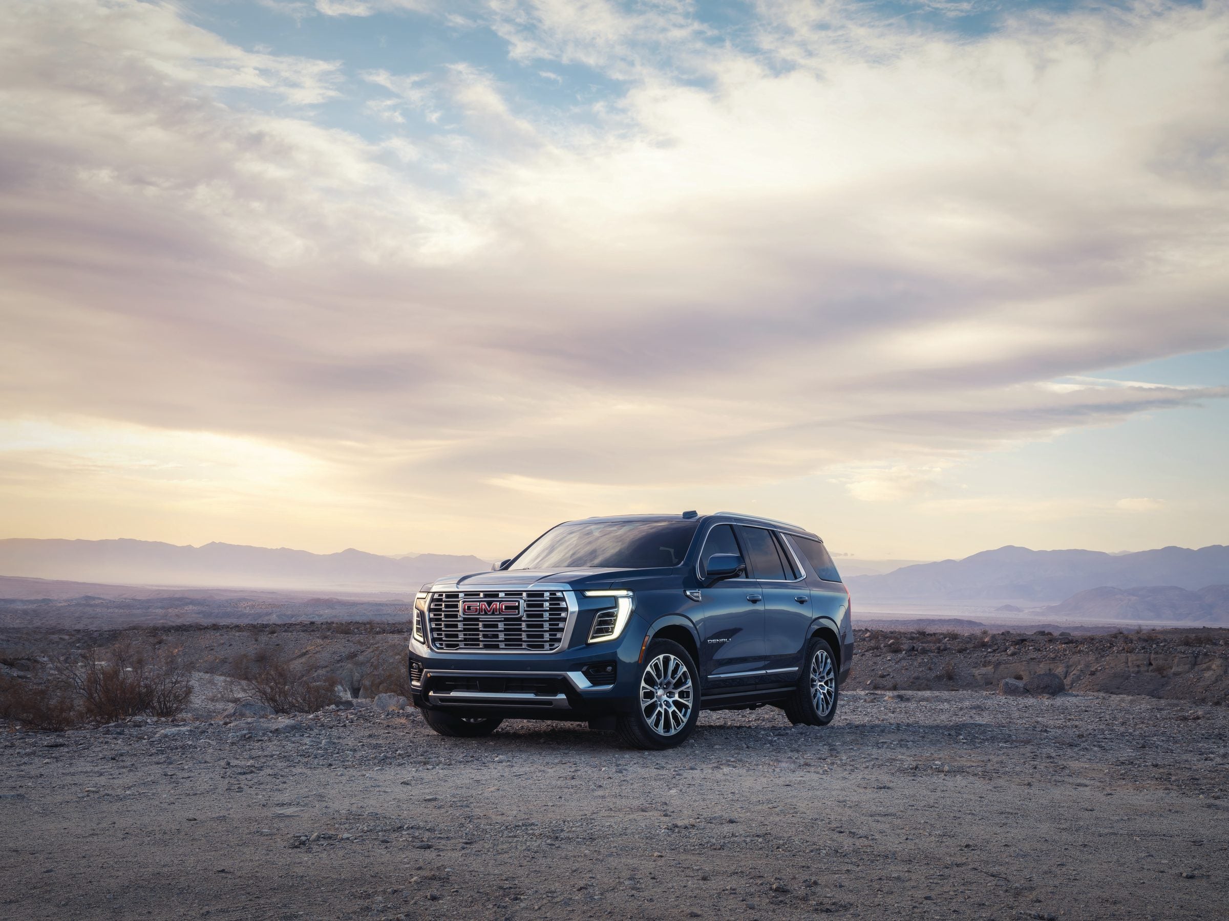 Blue GMC Yukon Denali parked on a gravel overlook with mountains under a wide evening sky