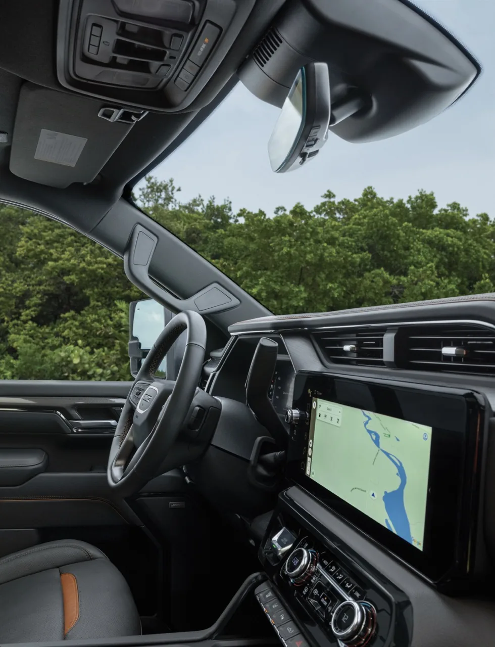 Driver-side view across the cabin of a GMC Sierra HD, showing the steering wheel and a tall touchscreen with a river map