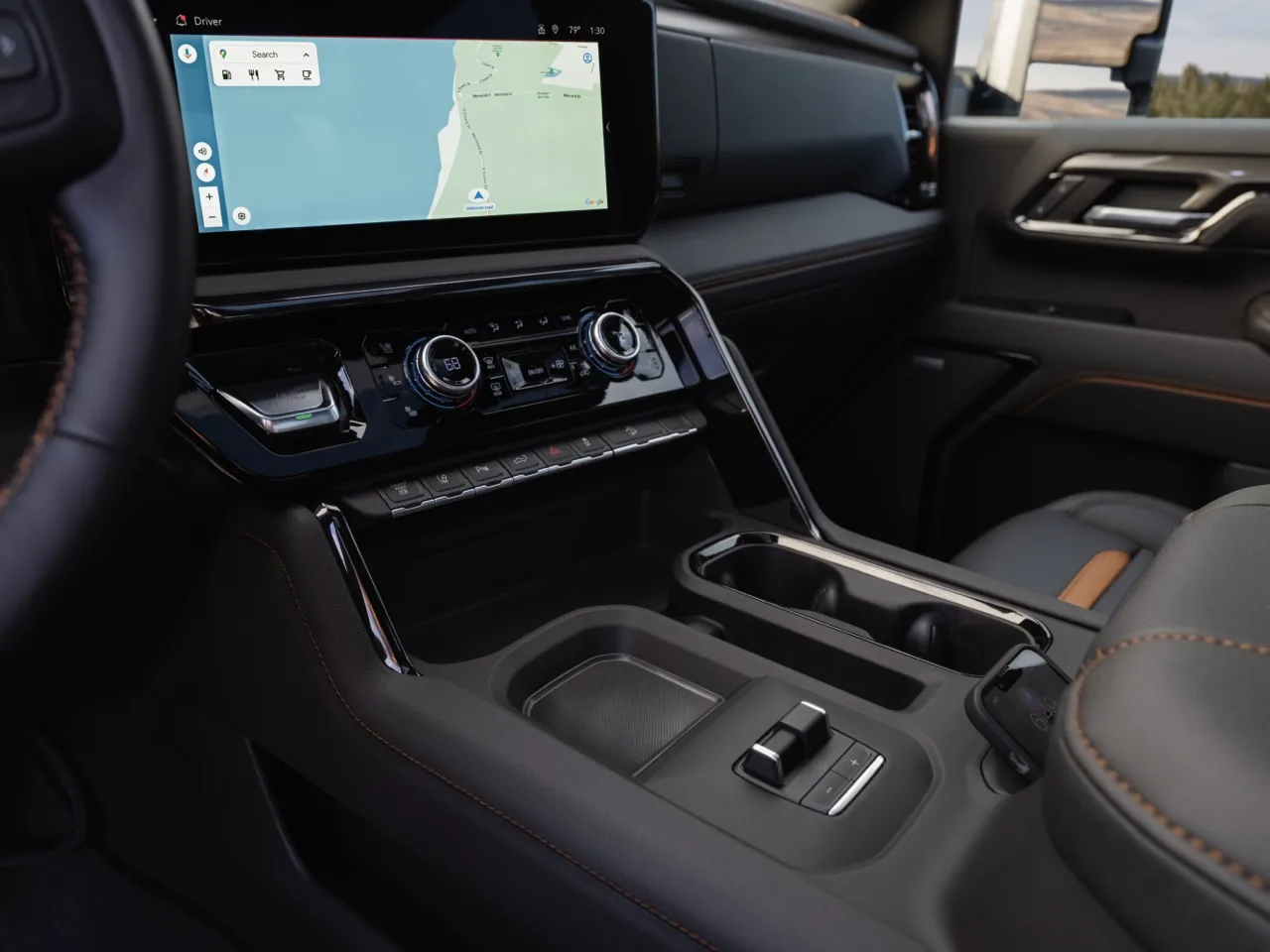 Center console and dashboard of a GMC Sierra HD with a map on the touchscreen, dual climate knobs and orange stitching on dark leather